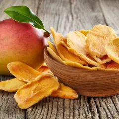 Un mango fresco e una ciotola di mango disidratato, che ne esaltano le proprietà nutritive e il sapore concentrato.