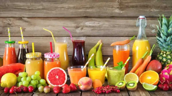 Varietà di bevande colorate e freschi estratti di frutta, con frutta intera e a fette su uno sfondo di legno.