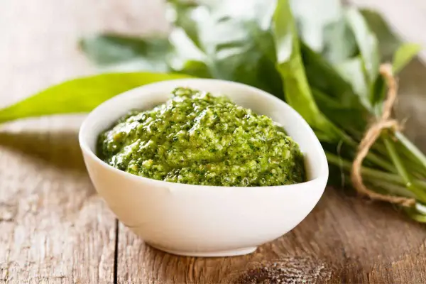 Pesto verde in una ciotola bianca, con un fascio di foglie di sedano fresche sullo sfondo. Perfetto per le tue ricette.